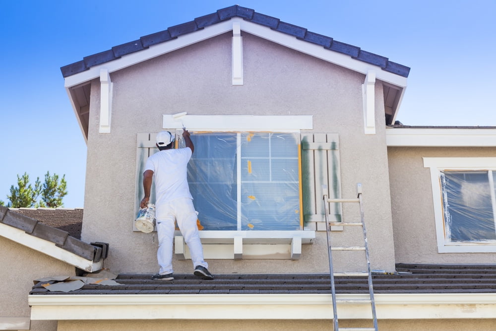 A man painting a window on a house.