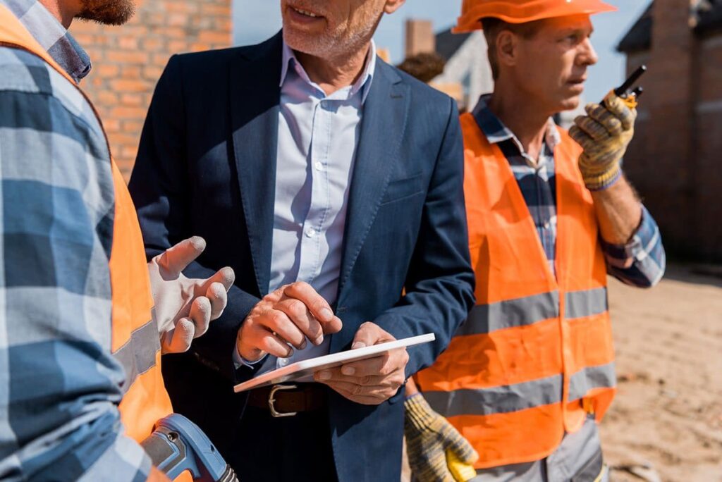 Three construction workers talking on a tablet in front of a construction site.