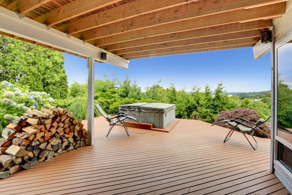 Cozy covered deck with jacuzzi and chairs. Deck has a beautiful nature view