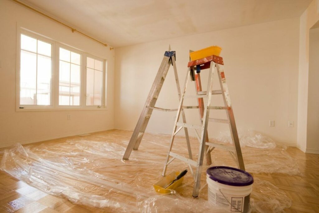 An empty room with paint on the floor and a ladder.