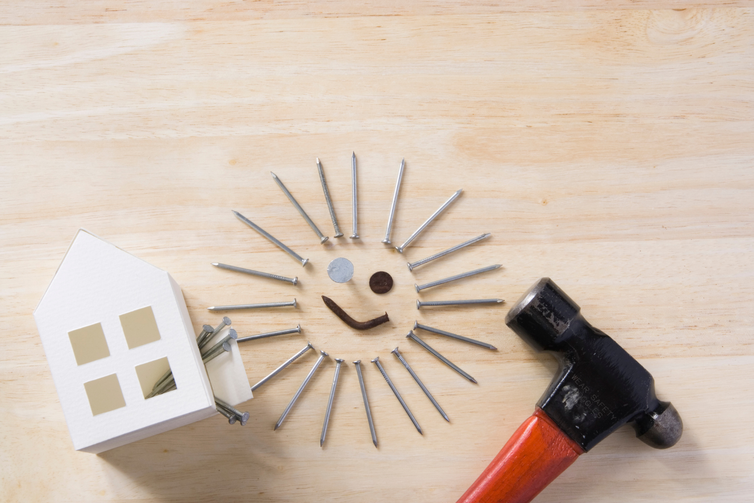 A hammer and a paper house on a wooden table.