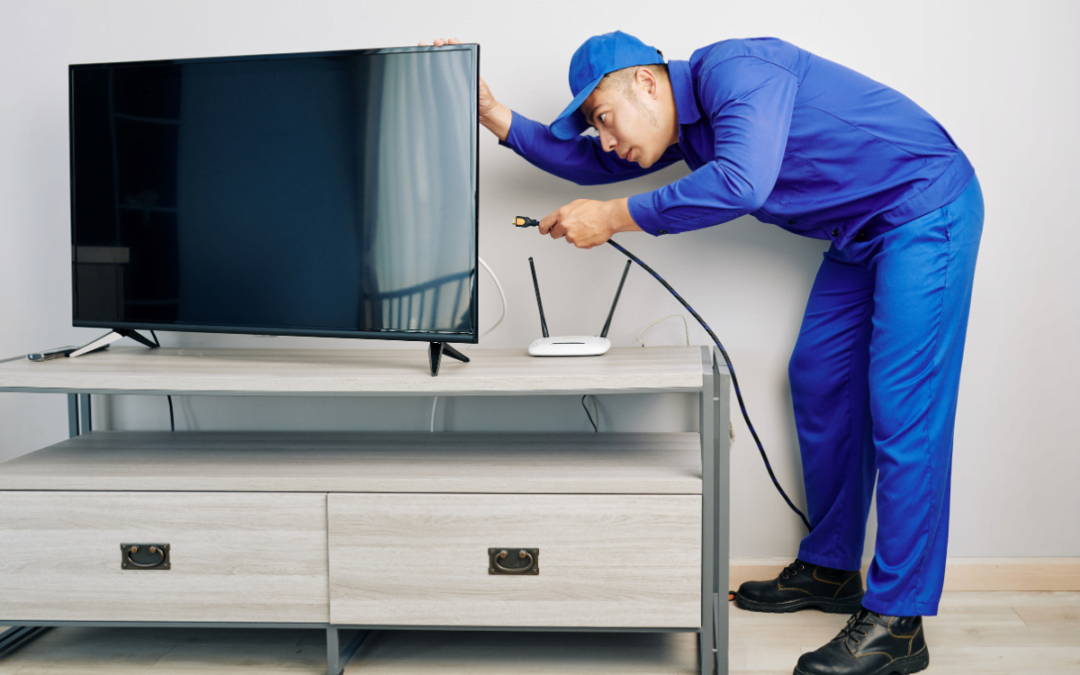 A man in blue skillfully hiding tv wires while working on a TV.