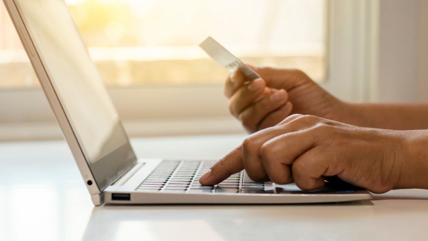 A hand holding a credit card while using a laptop for financing.