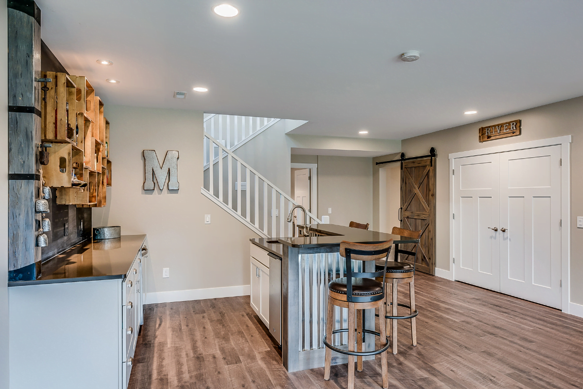 Johns Creek remodeling services showing a kitchen in a basement with a stylish bar area featuring sleek bar stools and an elegant staircase.