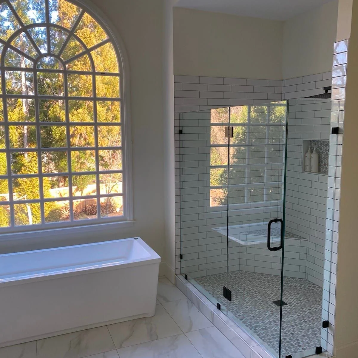 Bathroom Remodeling Services 21 Modern bathroom featuring a freestanding white tub, glass-enclosed shower with subway tile, and large window providing natural light, showcasing a blend of style and functionality for a luxurious remodel.