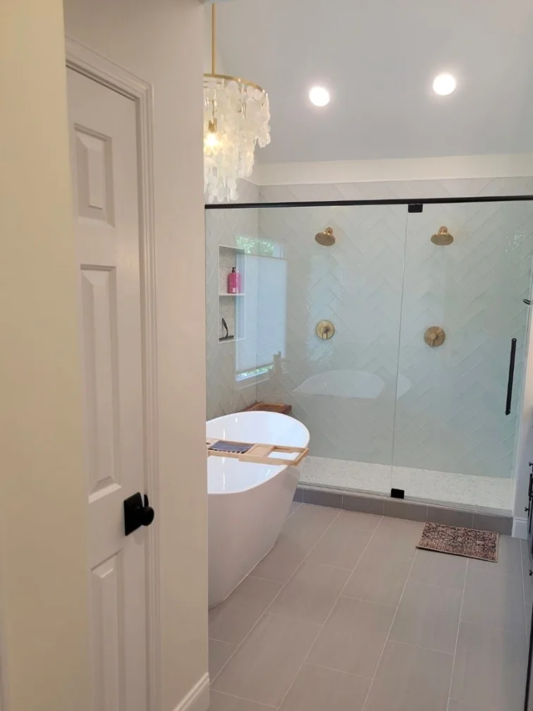 Bathroom Remodeling Services 23 Modern bathroom featuring a freestanding tub, glass shower with gold fixtures, herringbone tile design, and elegant chandelier, showcasing luxury and functionality in bathroom remodeling by FD Remodeling Atlanta.
