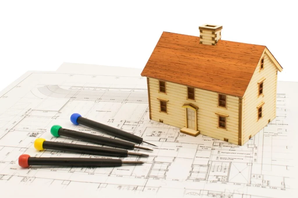 Remodeling Budget Breakdown: How to Make Every Dollar Count 3 A house on top of a blueprint with pens and pencils, representing an affordable remodeling project.