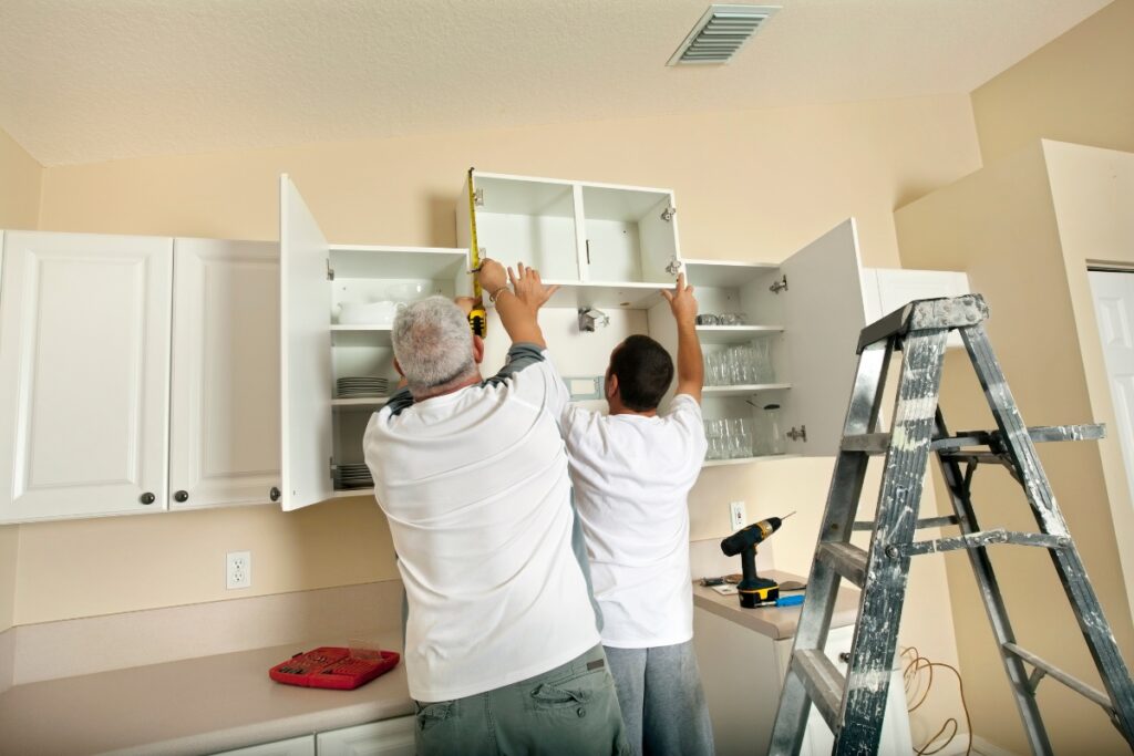 Two men working on a cabinet in a kitchen while adhering to a remodeling budget.