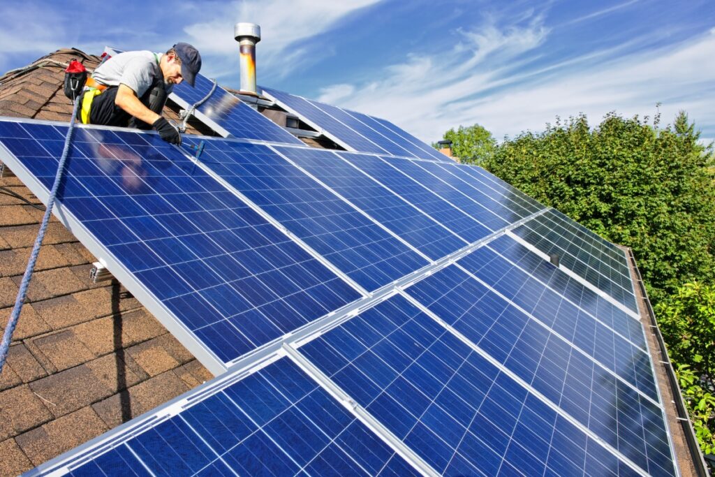 A man performing green building installation by installing solar panels on a roof.