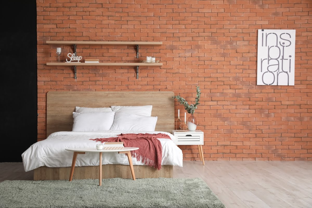 A bedroom bed with a rug and shelves in front of a focal brick wall.