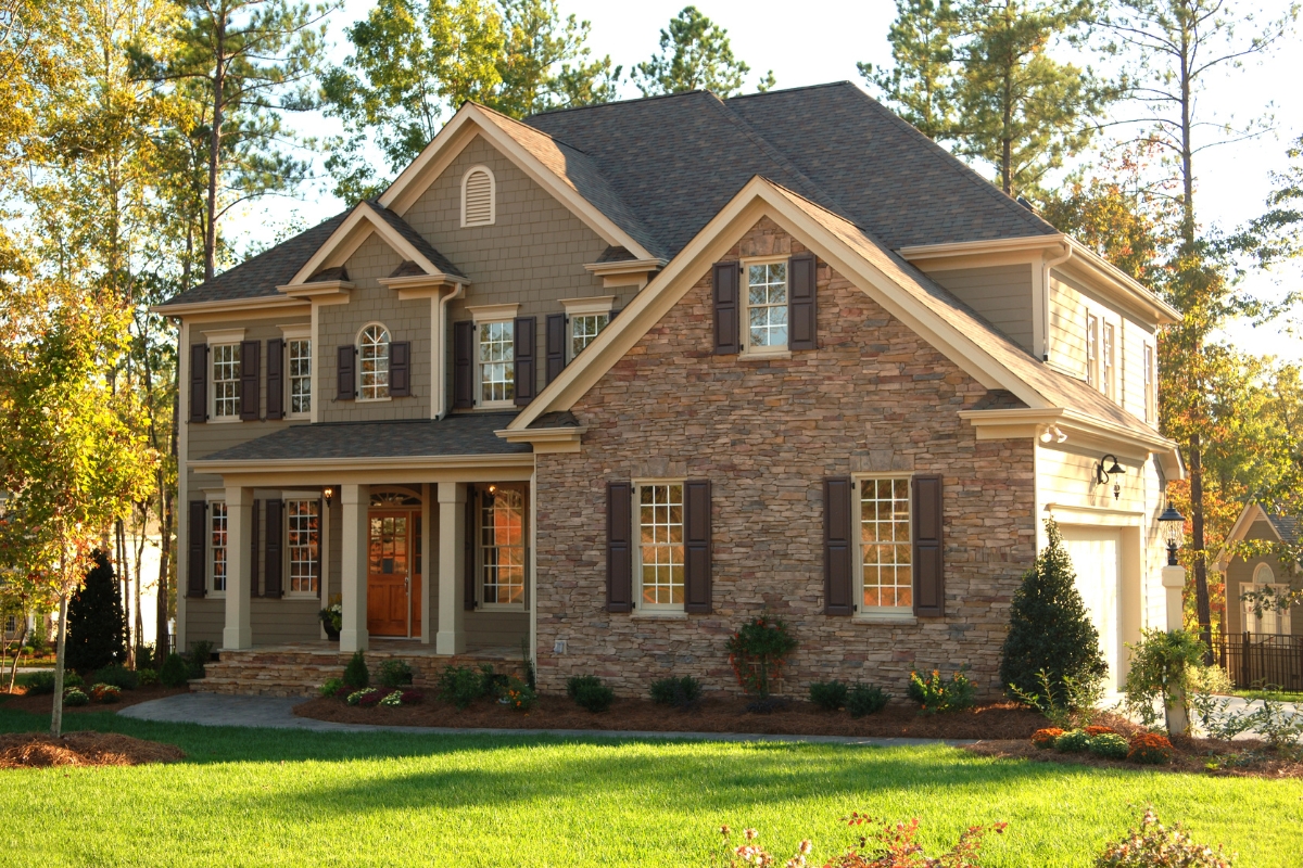 A two-story suburban house with stone and exterior design, featuring a covered entryway and manicured front lawn.