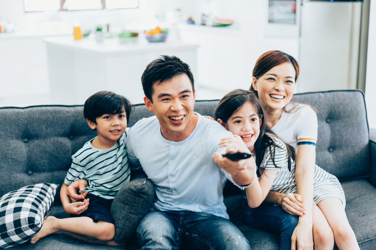 A man, woman, and two children sitting on a couch, hiding TV wires.