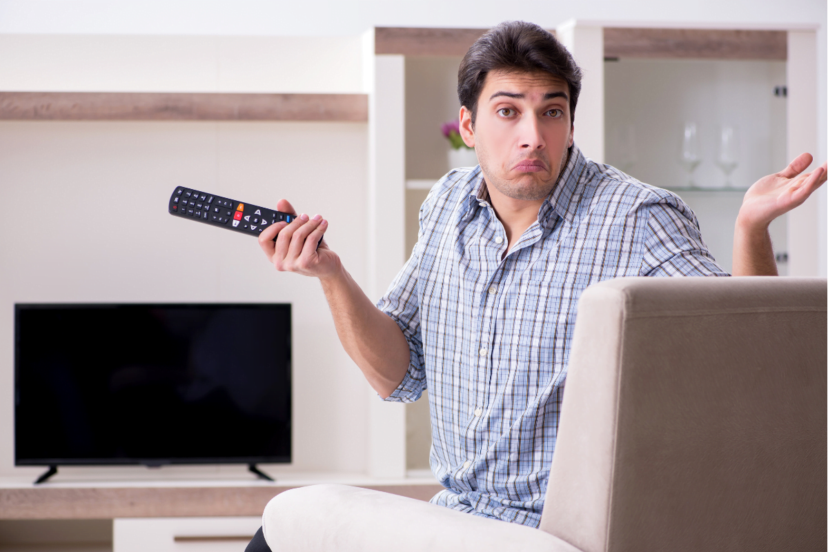 A man sitting on a couch holding a remote control, with no TV wires in sight.