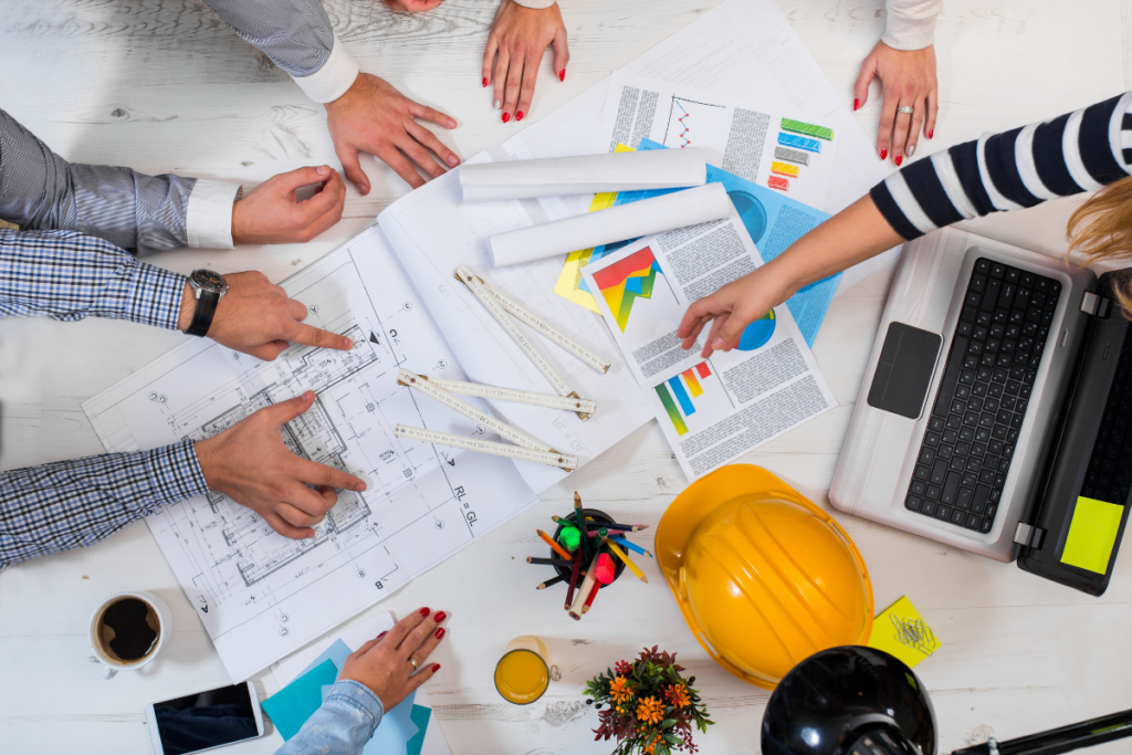 A group of people with hard hats engaging in project management around a construction table.