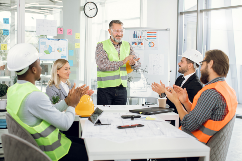 A group of construction workers clapping at a project management meeting.