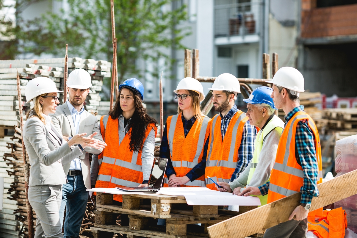 A group of construction workers and an engineer in safety gear having a discussion on safety standards in construction on a construction site.