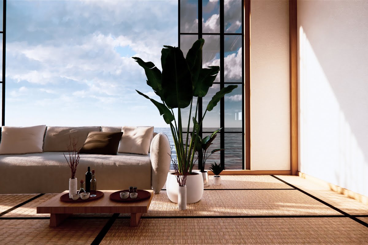 A minimalist living room with a large sofa, a low wooden coffee table, and potted plants, featuring floor-to-ceiling windows showcasing an ocean view. Tatami mats cover the floor, enhancing the home's aesthetic charm commonly celebrated in interior decorating.