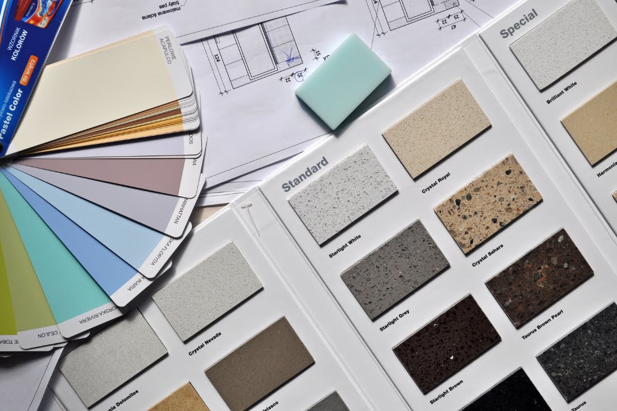 A variety of countertop samples and paint swatches are displayed alongside architectural plans and a blue paint sample block, showcasing the careful consideration of home aesthetics in interior decorating.