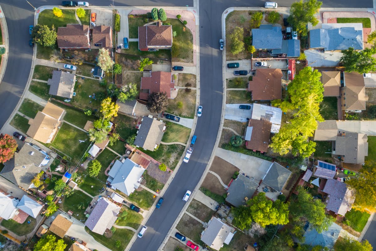 Aerial view of a suburban neighborhood with distinct houses, driveways, and roads, showcasing varied roof colors and landscaped yards, reflecting current real estate market trends.