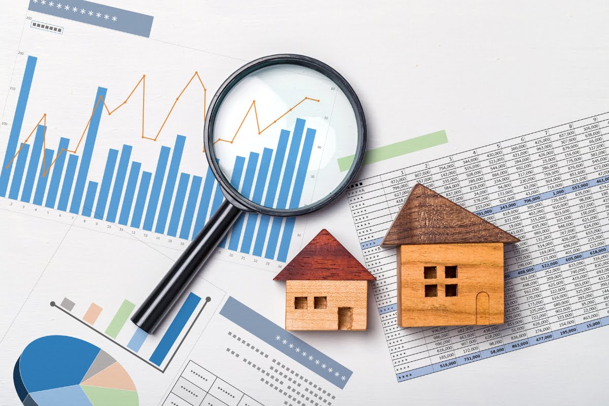 Magnifying glass focusing on printed charts with wooden house models on financial documents, symbolizing real estate market trends analysis.