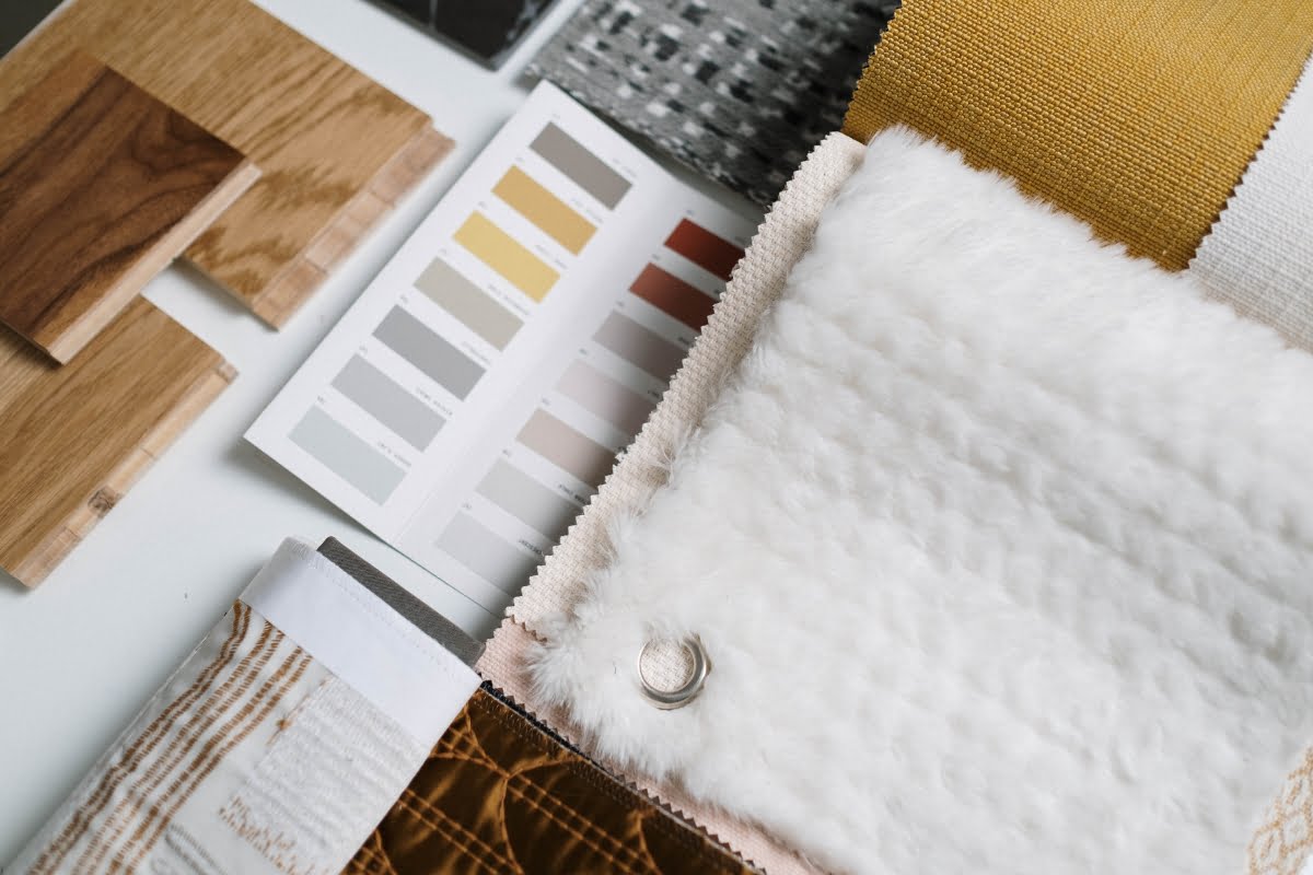 A collection of interior design samples, including wood textures, fabric swatches, and a color palette card, is displayed on a white surface, perfect for gathering DIY home improvement tips.