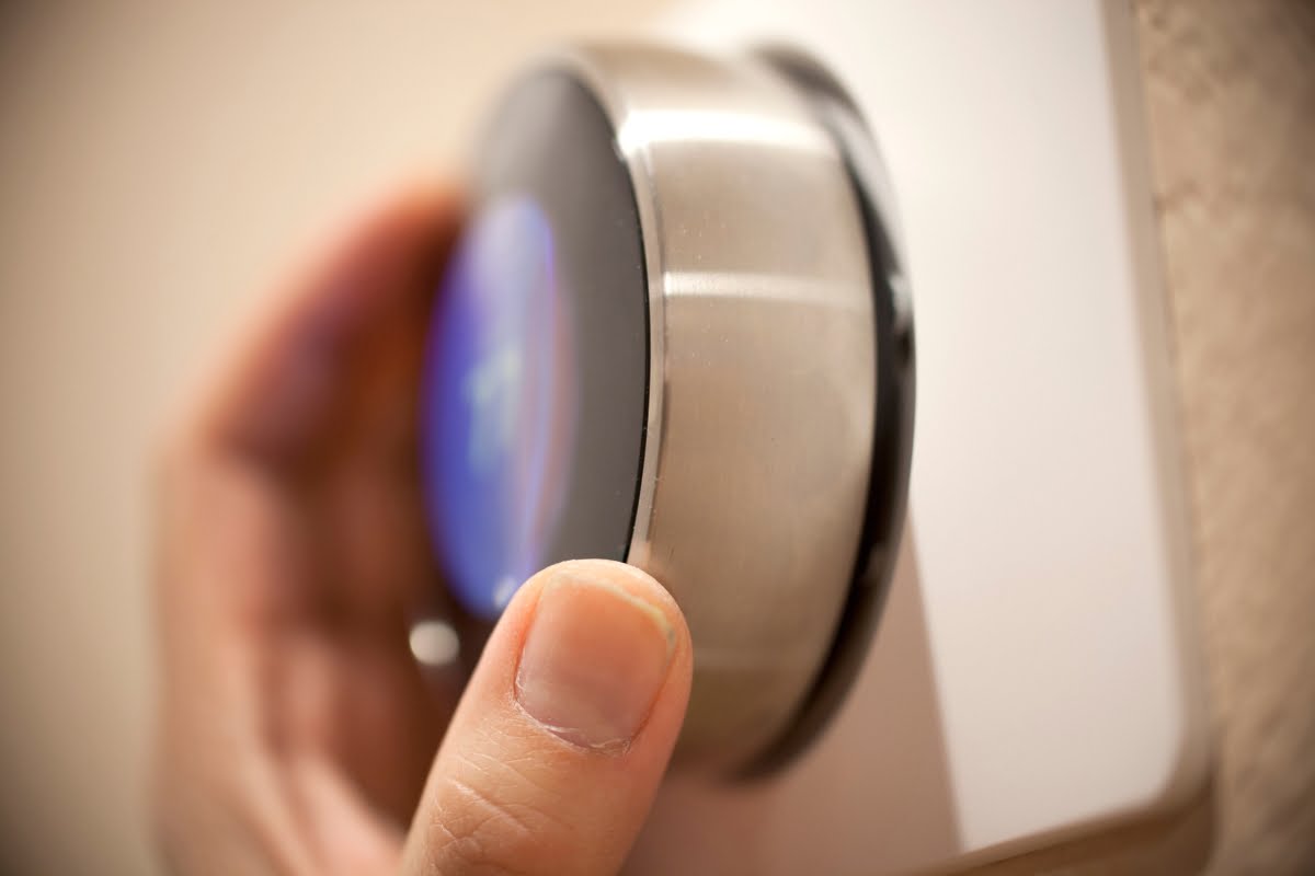 Hand adjusting a modern, stainless steel smart thermostat, showcasing the latest in Smart Home Technology, mounted on a white wall.