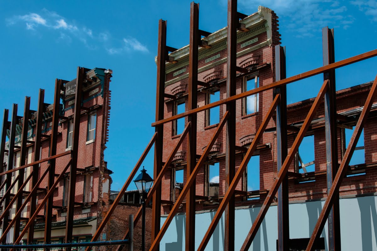 Partially demolished brick buildings with steel support beams showcase the importance of building preservation, set against a bright blue sky.