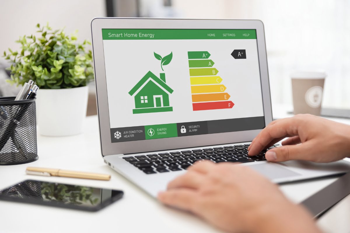 Person using a laptop displaying a smart home energy management system with an energy efficiency rating chart. The setup, focused on promoting energy efficiency in homes, includes a green plant and a coffee cup visible in the background.