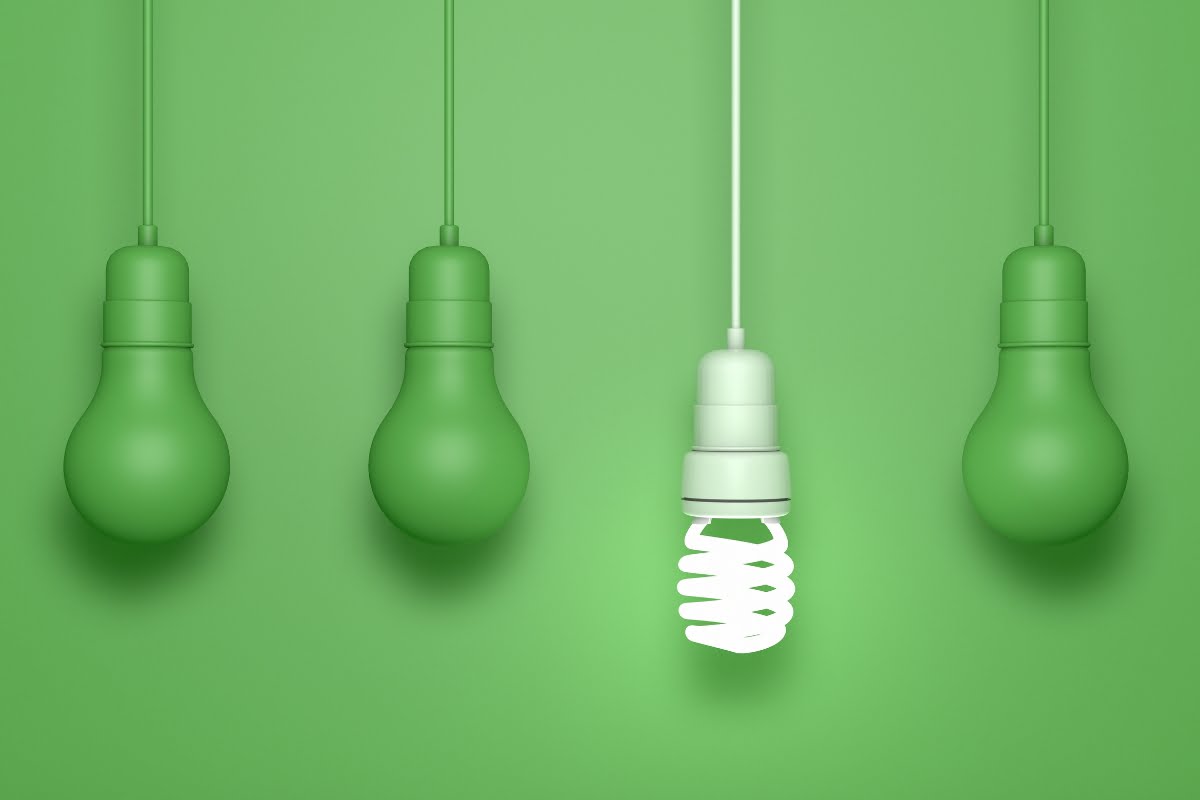 Image of five hanging light bulbs against a green background. The first, second, fourth, and fifth bulbs are traditional incandescent bulbs. The third bulb highlights energy efficiency in homes with its glowing compact fluorescent light bulb.