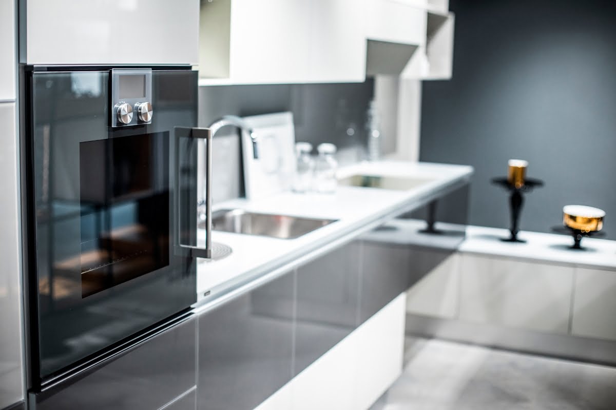 Modern kitchen with sleek white cabinets, stainless steel oven, and a double sink. The countertops are clutter-free, showcasing exquisite furniture design with two decorative items near the sink.