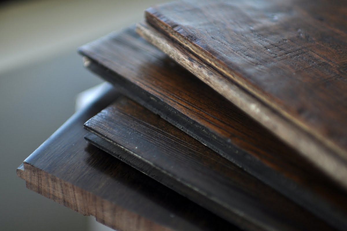 Close-up of a stack of various wooden planks with different shades and grain patterns. The image focuses on the edges, showcasing the texture and thickness of these sustainable building materials.