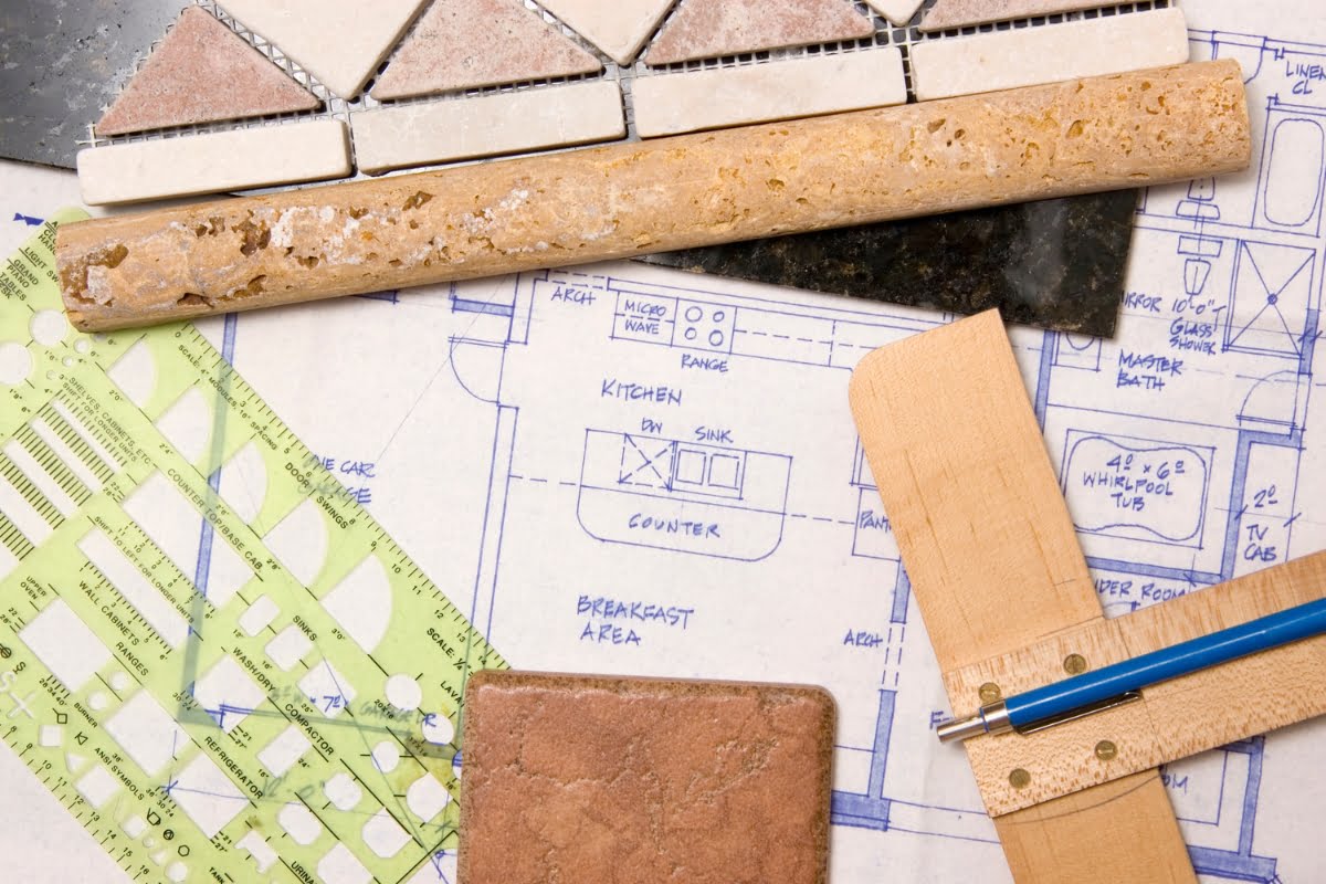 Architectural blueprints and design tools, including ruler, templates, tiles, and countertop samples, are meticulously arranged on a table for a home investment kitchen renovation project.