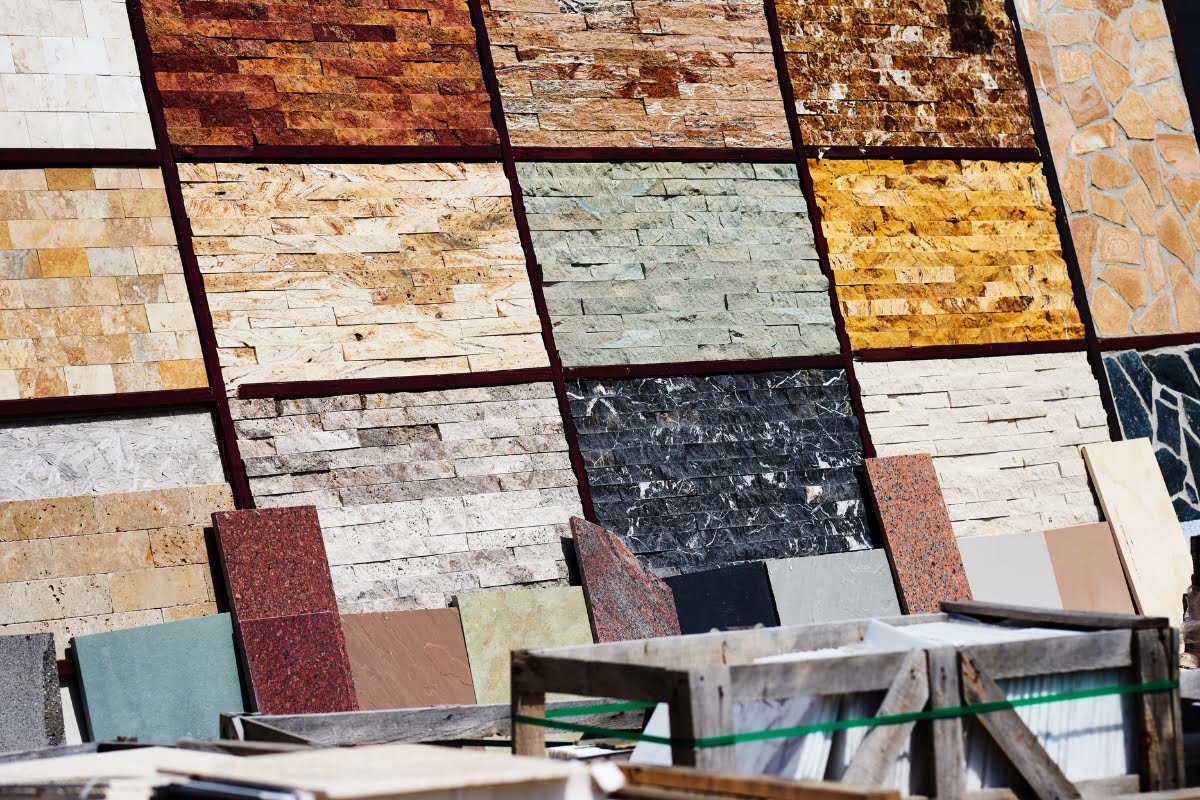 A variety of stone and tile samples are displayed on a wall, showcasing different colors and textures, arranged in a grid pattern. Construction materials are placed in the foreground, highlighting options for your next home investment.