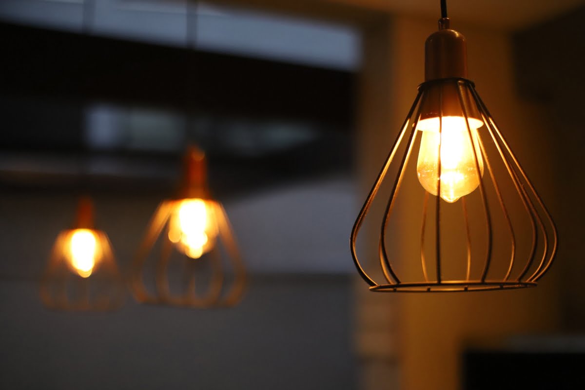 Three pendant lights with wire cage covers hang from the ceiling, each emitting a warm, soft glow—a true home investment. The background is blurred.