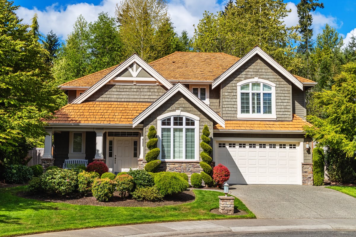 A prime home investment, this two-story suburban house features a landscaped garden, gray exterior, white trim, and a shingled roof.