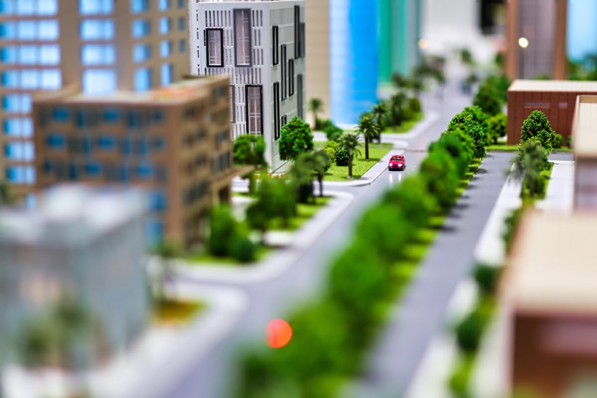 A detailed scale model of a modern urban neighborhood featuring high-rise buildings, trees, and a red car on a road, skillfully designed to showcase exceptional urban planning.