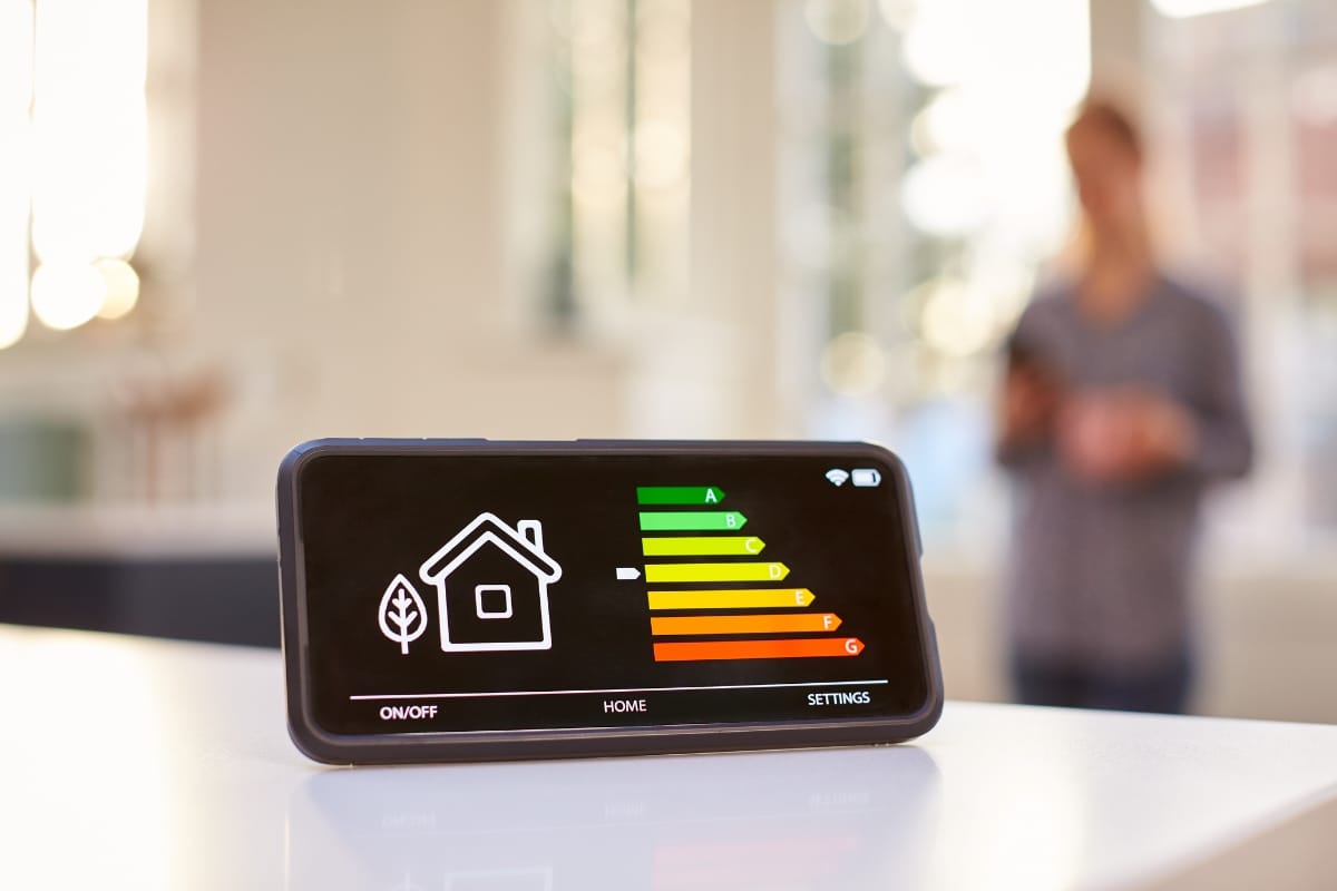 A smartphone displays an energy efficiency chart, highlighting the benefits of energy efficient remodeling, with a house icon prominently in the foreground and a person blurred in the background.