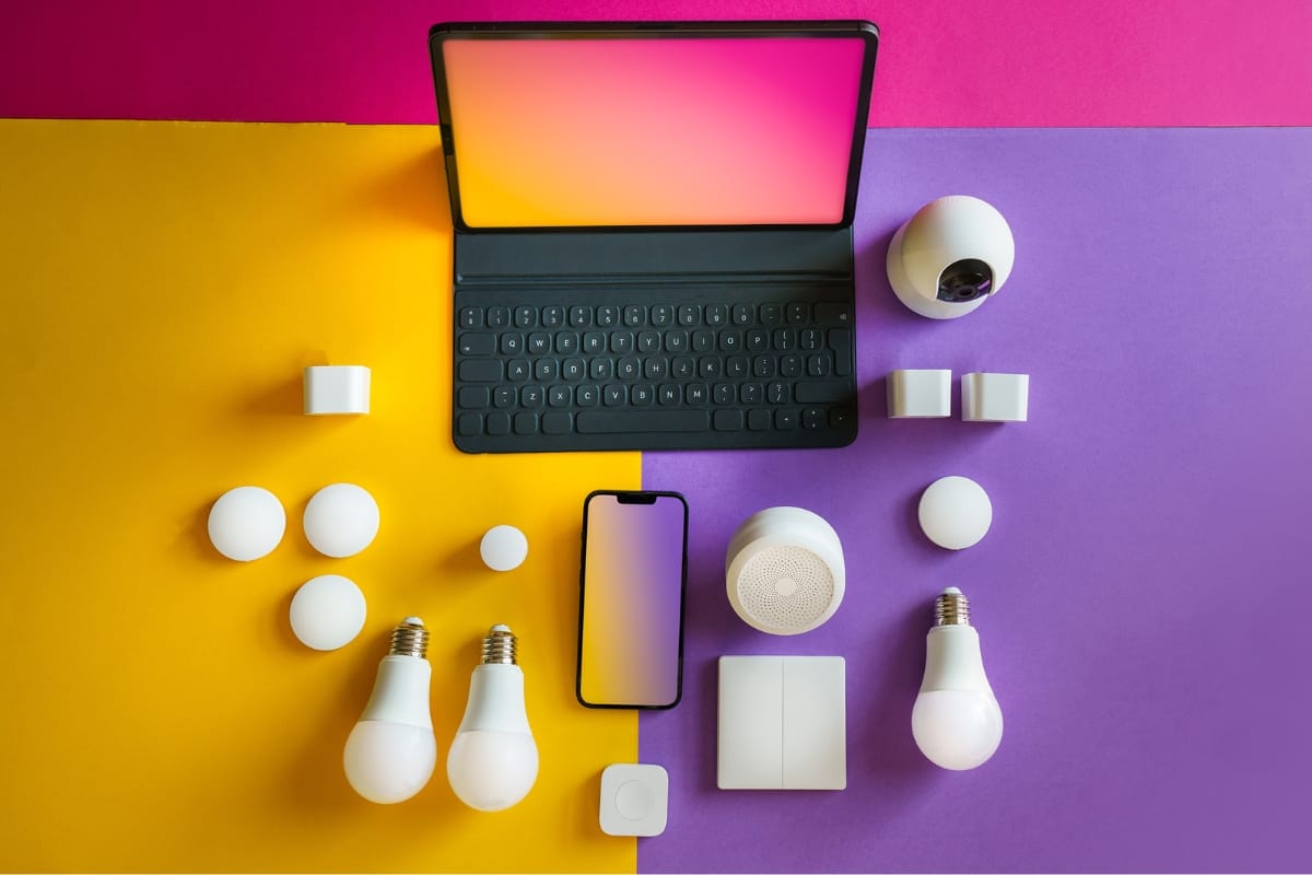 A tablet and smartphone surrounded by smart home devices, including bulbs, sensors, and cameras, set against a yellow and purple background—a perfect blend for exploring home accessibility remodeling.