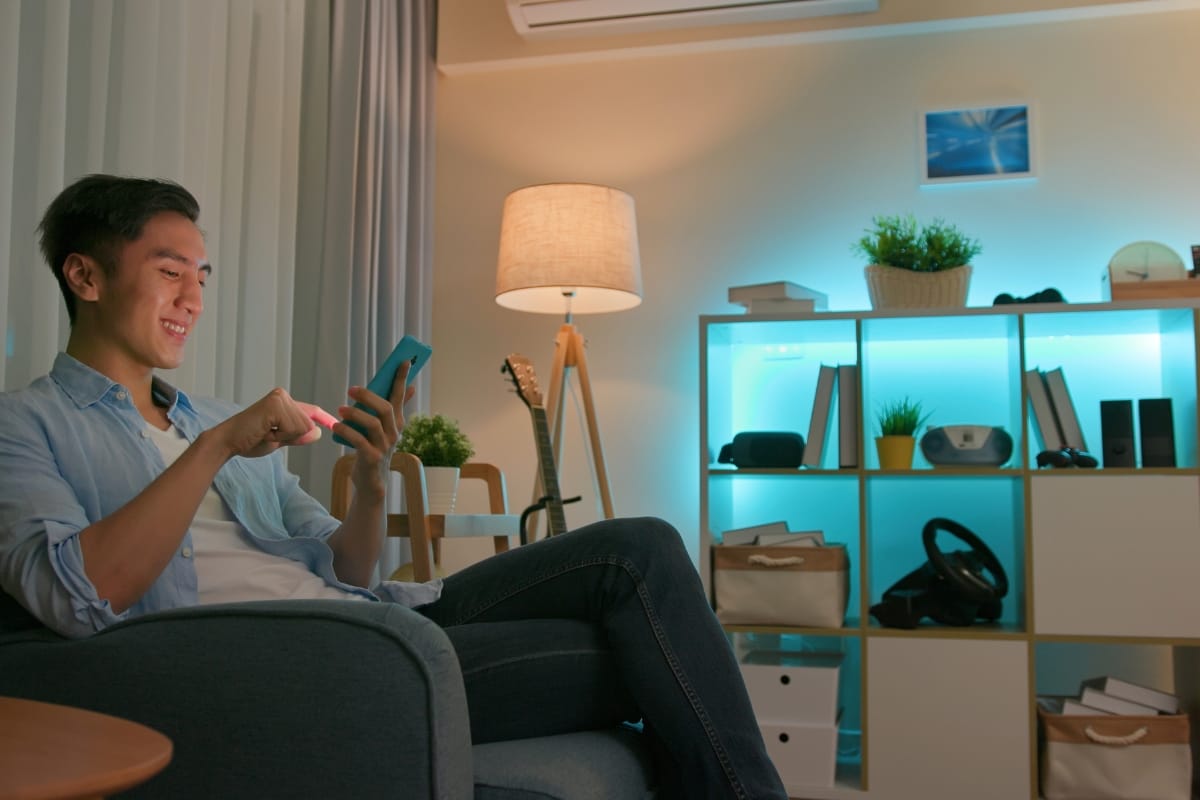 A person relaxes on a sofa in a cozy, accessible living room, using a smartphone. Shelves with books, a plant, and decorative items create an inviting background that blends style with thoughtful design.