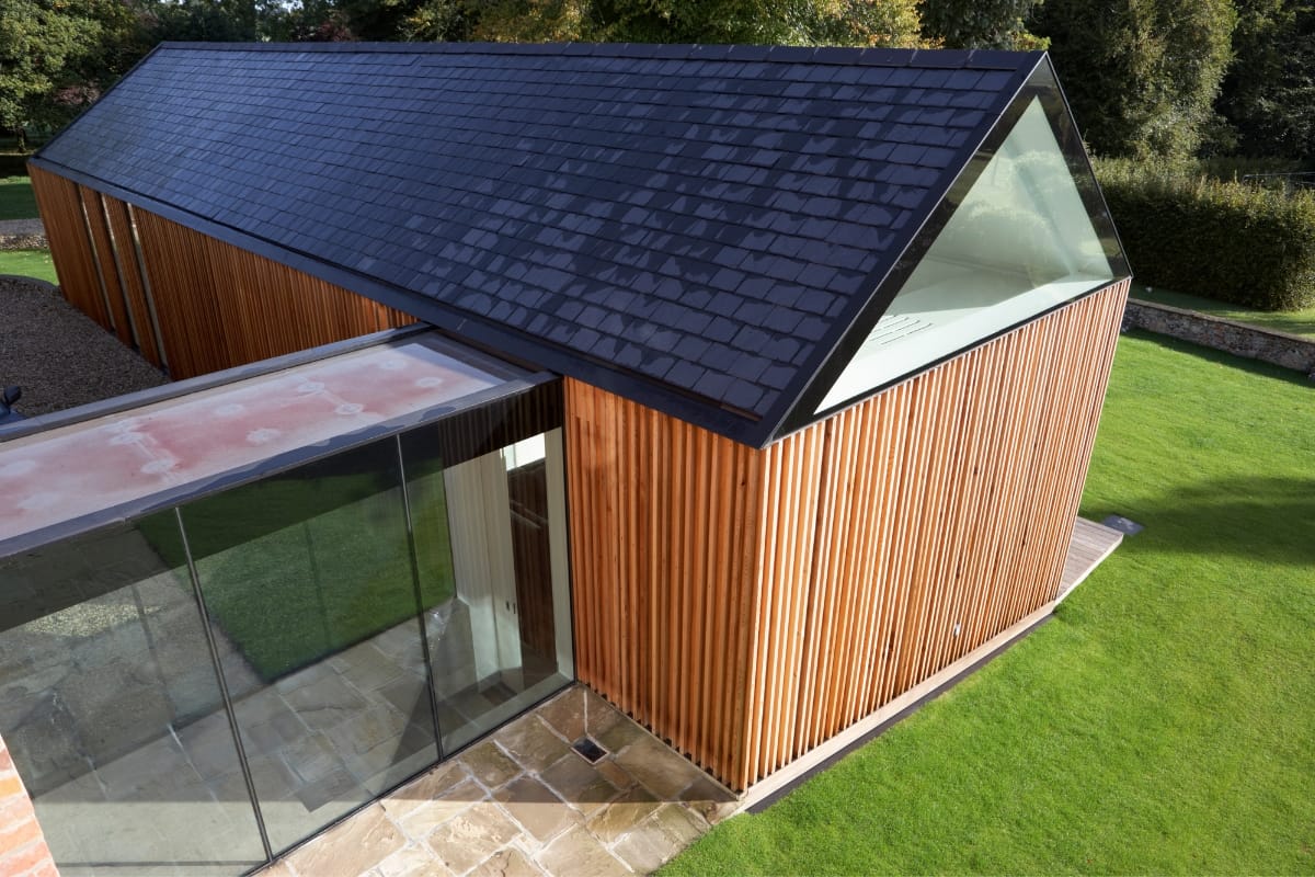 Modern building with a glass and wood exterior, featuring a sloped slate roof and large glass surfaces. This stylish structure, potentially serving as an accessory dwelling unit, is surrounded by a lush green lawn.