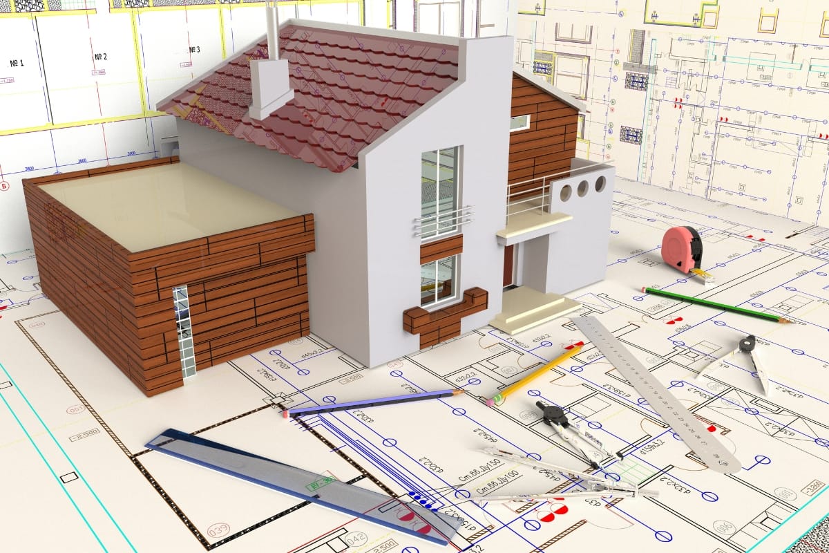 A small architectural model of an accessory dwelling unit sits on top of detailed blueprints, surrounded by rulers, pencils, and drafting tools.