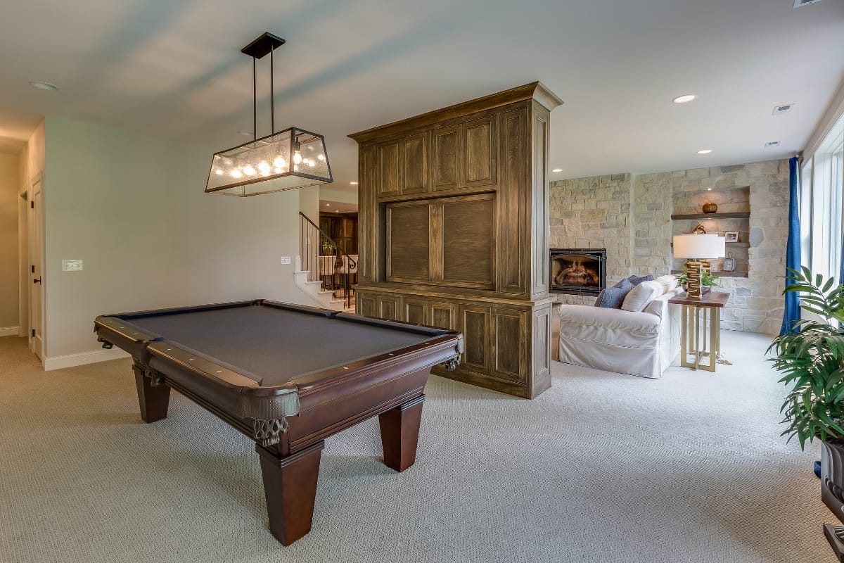 Considering whether you should finish your basement? Picture a cozy space with a wooden pool table, a large wood entertainment unit, a fireplace, and a comfy seating area with a couch. Transform your basement into the ultimate retreat.