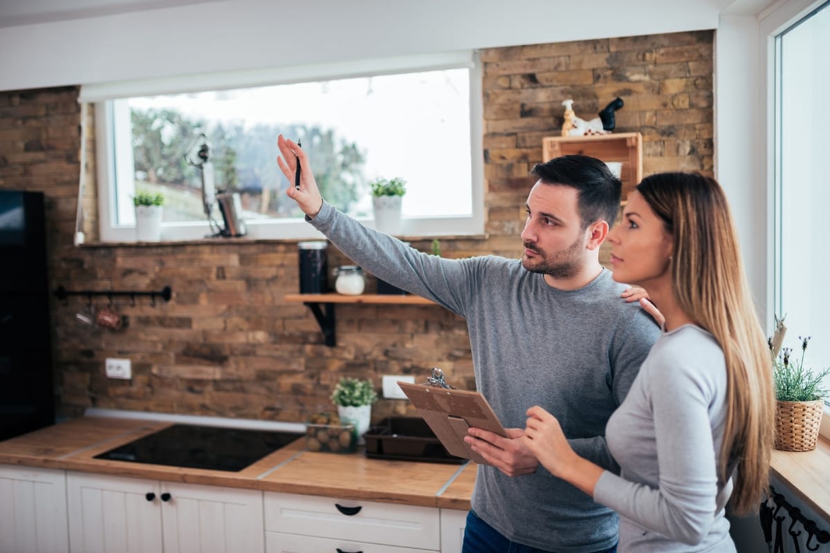 Step-by-Step Remodeling Process: How to Renovate Your Roswell Home Seamlessly 2 A man holding a clipboard gestures towards something in a modern kitchen, guiding a woman through the remodeling process as they both look in the same direction.