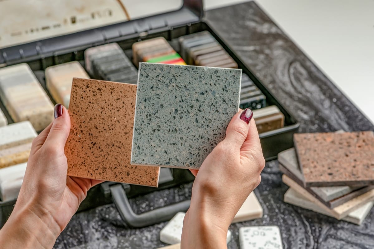 Step-by-Step Remodeling Process: How to Renovate Your Roswell Home Seamlessly 4 Hands holding two countertop material samples over a display case with various other samples on a black marble surface—an essential step in the remodeling process.