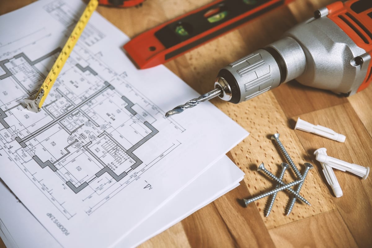 Step-by-Step Remodeling Process: How to Renovate Your Roswell Home Seamlessly 1 A floor plan rests on a table with a drill, screws, wall anchors, tape measure, and level, capturing the essentials needed for the remodeling process or renovation work.