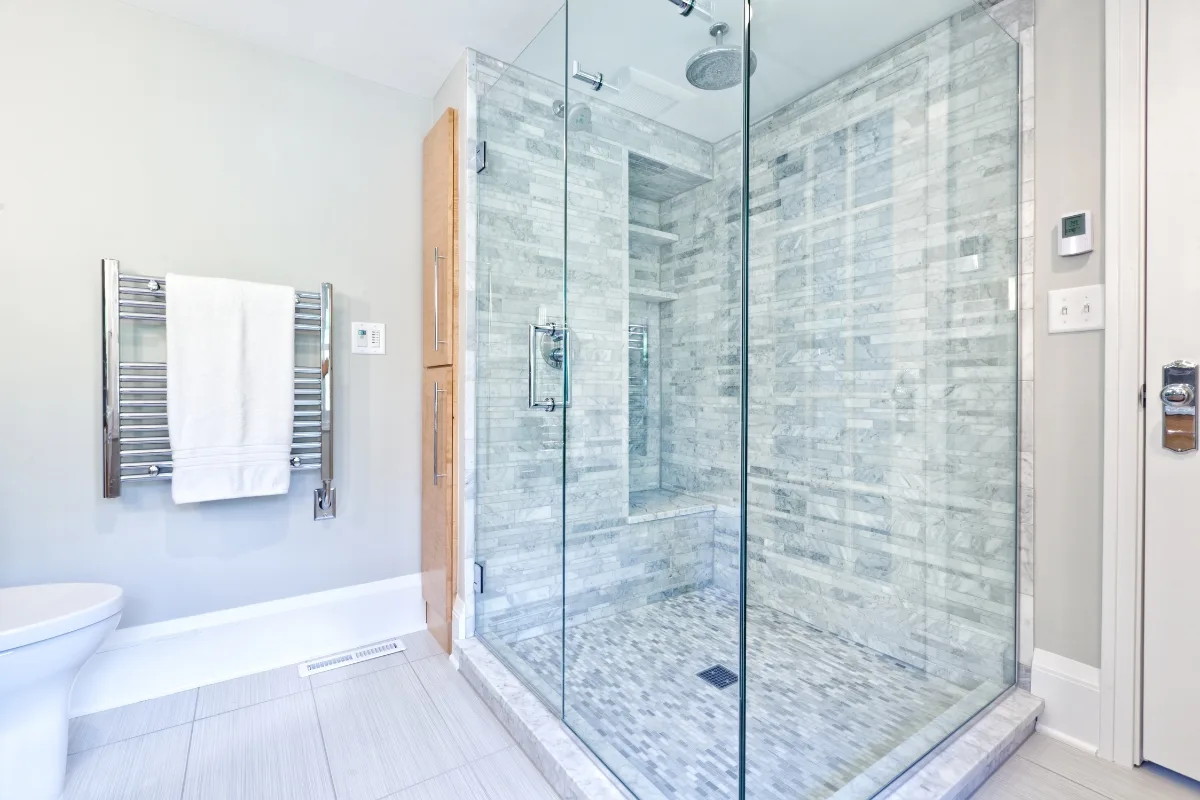 Modern bathroom remodeling with a large glass-enclosed shower featuring gray tile, a wall-mounted towel warmer with a white towel, and a sleek white toilet.