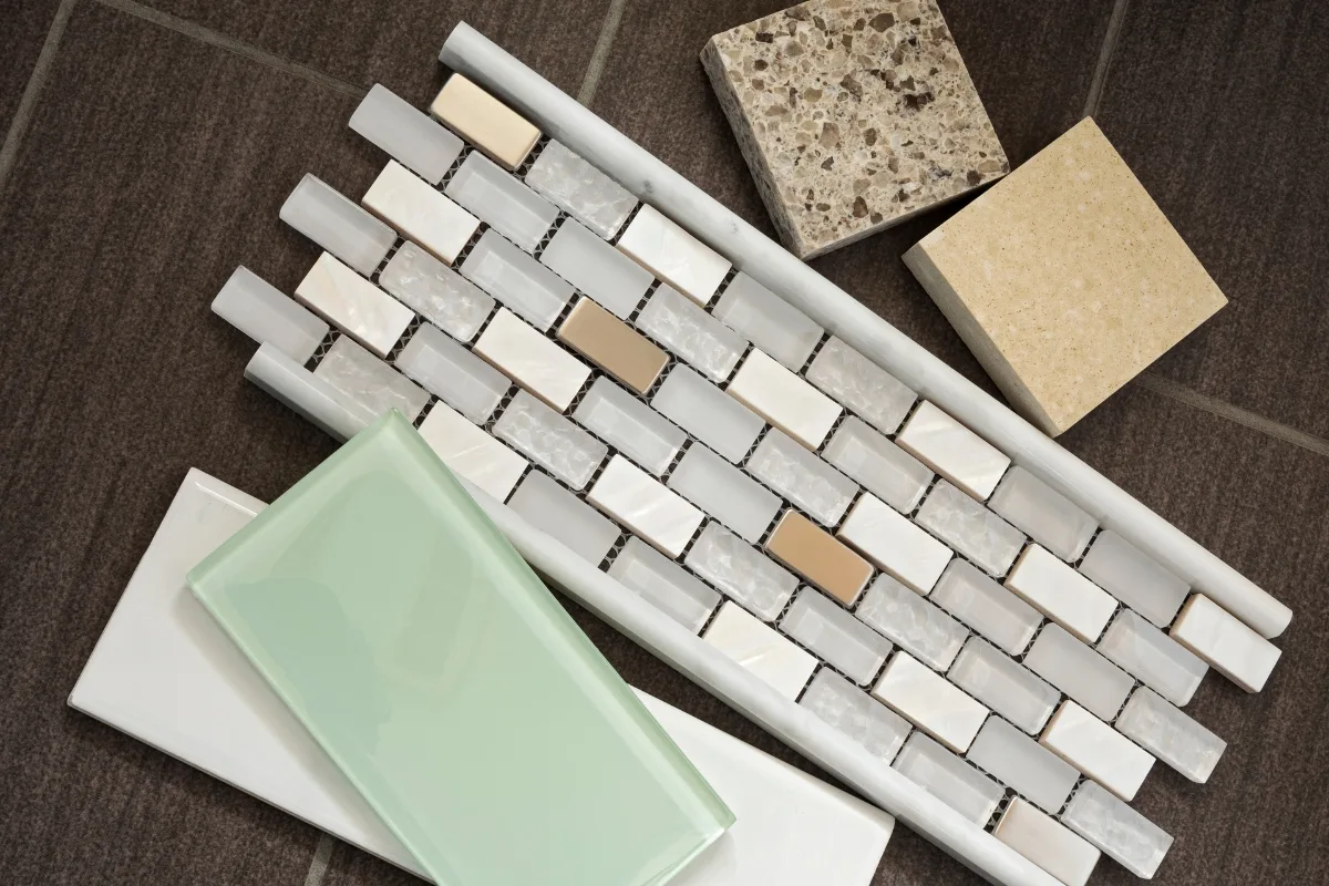 Assorted samples of tile, mosaic, and stone arranged on a dark surface, showcasing various textures and neutral colors—perfect inspiration for your next bathroom remodeling project.