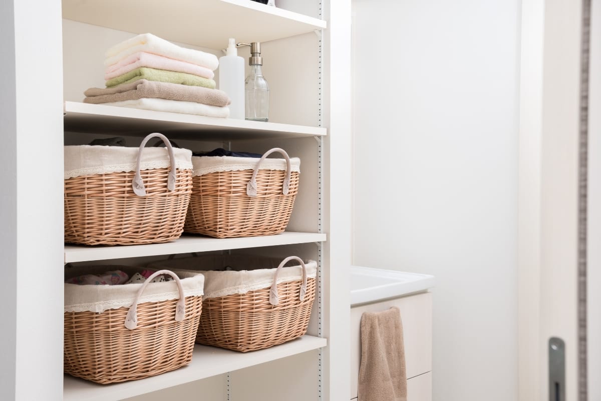 Bathroom Remodeling in Marietta: Space-Saving Ideas for Small and Modern Bathrooms 1 Open shelving in a laundry room showcases folded towels, wicker storage baskets, and a soap dispenser by the sink with a beige towel—perfect inspiration for your next bathroom remodeling project.