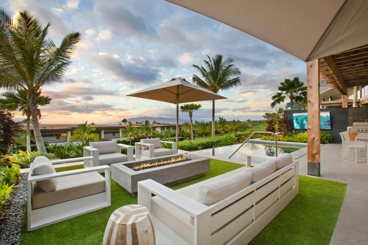Modern outdoor patio with white furniture around a rectangular fire pit, overlooking a pool and landscaped garden at sunset—a perfect setting for those who appreciate stylish outdoor patios.