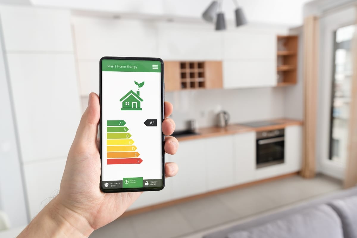 Smart Home Remodeling in Sandy Springs: Top Energy-Efficient Upgrades 1 A hand holds a smartphone displaying a smart home energy efficiency app in a modern kitchen, showcasing the benefits of smart home remodeling.